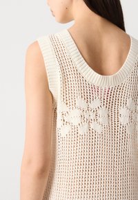 White, knitted sleeveless top with a wide neckline, featuring a floral pattern integrated into the mesh design and ribbed edges.