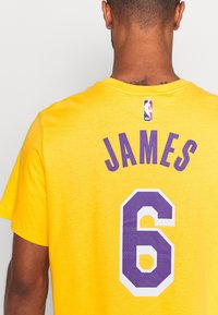 Keltainen lyhythihainen pelipaita, jossa on violetti teksti "JAMES" numeron "6" yläpuolella valkoisena, ja kauluksessa pieni NBA-logo.