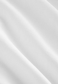 Biela látka s jemnou medovou štruktúrou vytvára mäkké diagonálne záhyby.