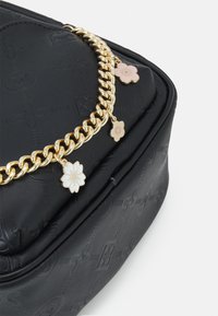Černá kožená taška s vyraženými květinovými vzory, vybavená zlatým řetízkovým popruhem ozdobeným růžovými a bílými květinovými přívěsky.