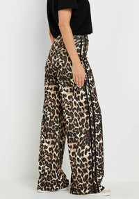 Pantalon large en imprimé léopard, fabriqué dans un tissu texturé avec des rayures noires sur les côtés, présentant une coupe décontractée et une taille haute.
