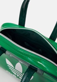 Zelená lakovaná kabelka s dvěma uchy, zipovým uzávěrem a vnitřní podšívkou. Na vnější straně se nachází bílé logo a stříbrný zip.