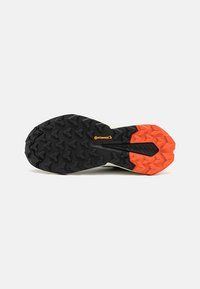 Shoe sole featuring a black rubber base with orange accents. Tread design includes multi-directional lugs for traction and stability.