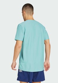 Camiseta de manga corta color azul claro con cuello redondo. Textura suave y corte holgado, presenta un patrón sutil. Llevada con pantalones cortos azul marino.