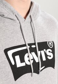 Primer plano de una sudadera gris con un logo de Levi's en blanco y negro en el pecho y cuerdas visibles colgando.