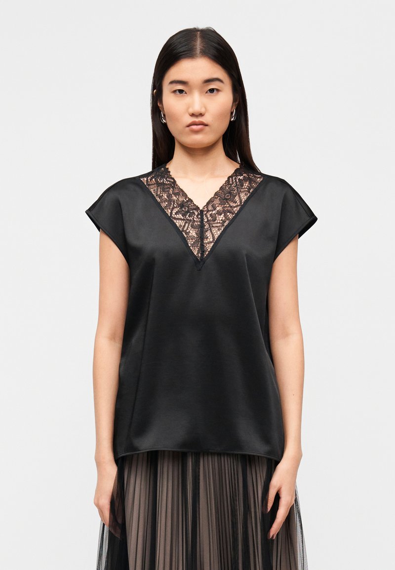 Μαύρο σατέν τοπ με δαντελωτή V-λαιμόκοψη, κοντά μανίκια και άνετη εφαρμογή. Η υφή είναι λεία με κομψές λεπτομέρειες στη λαιμόκοψη.