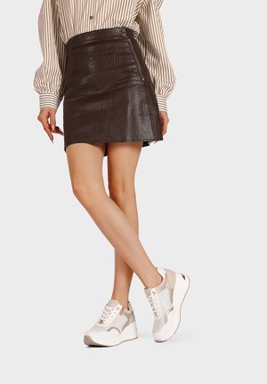 Gonna mini in pelle marrone con un design strutturato, abbinata a sneakers bianche e beige con dettagli in rete e suola spessa.