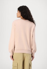 Lys rosa sweatshirt med rund hals og ribbede mansjetter. Stoffet er mykt og glatt, med et enkelt, uornamentert design.