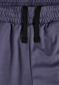 Lila sportiga joggingbyxor med en slät yta, elastisk midja och svart dragsko. Har veckad tyg vid midjan för en åtsittande passform.