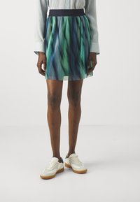 Fållad kjol med en figurnära marinblå midja, som har en gradient av blå och gröna färger. Kombinerad med vita sneakers och textil med struktur.