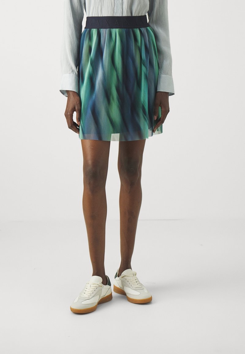 Fållad kjol med en figurnära marinblå midja, som har en gradient av blå och gröna färger. Kombinerad med vita sneakers och textil med struktur.