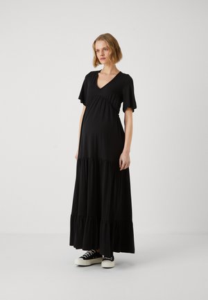 Schwarzes Maxikleid mit tiefem V-Ausschnitt, kurzen Ärmeln und gerafftem Taillenzug. Besitzt einen gestuften Rock und wird mit schwarzen Sneakers kombiniert. Weicher Stoff.