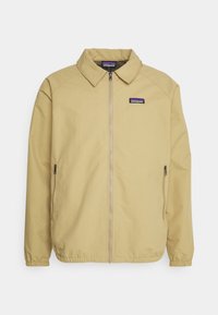 Light beige jacket with a collared neckline, zip front, and elastic cuffs. Features side pockets and a small logo patch on the upper left.