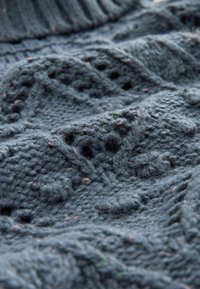 Stickad tröja i mörkgrå ull, med texturerade mönster och upphöjda samt öppna stygndesigns, mjuk finish och subtila färgfleckar.