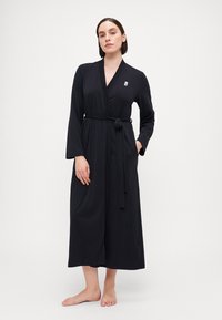 Robe noire à manches longues et enveloppantes, en tissu doux, avec une ceinture à la taille. Présente un petit logo sur la poitrine et un ourlet droit.