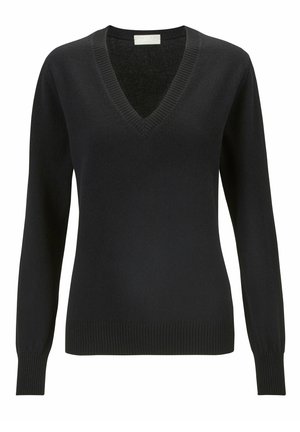 Suéter negro de cuello en V, diseño ajustado, combinado con pantalones jogger gris oscuro con aberturas laterales y zapatillas blancas sobre un fondo claro.