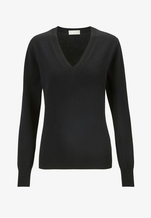 Suéter negro de cuello en V, diseño ajustado, combinado con pantalones jogger gris oscuro con aberturas laterales y zapatillas blancas sobre un fondo claro.