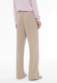 Beige wide-leg pants with an elastic waistband, made from a smooth fabric, featuring a relaxed fit and subtle texture.