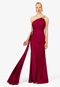 Einseitiges Abendkleid in tiefem Magenta mit drapiertem Stoff, einem hohen Schlitz und verzierten Details an der Schulter. Glatte Textur.