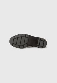 Suola di scarpa in gomma nera con un motivo di grip testurizzato, caratterizzata da una forma curvata e una finitura liscia vicino al tallone.
