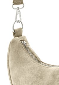 Dettaglio di una borsa a spalla in suede beige con zip e hardware in argento, dalla forma curvata e superficie testurizzata. Include una tracolla regolabile.