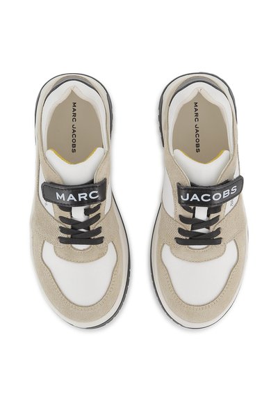 Paire de baskets beige et blanc avec des lacets noirs et des sangles noires estampillées "MARC" sur la gauche et "JACOBS" sur la droite.