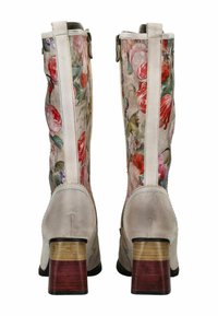 Un paio di stivali al ginocchio con motivo floreale, dettagli in pelle beige, tacchi a blocco in tonalità di legno stratificate, visti da dietro.