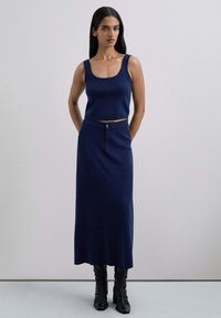 Top de punto ajustado en azul marino, combinado con una falda larga a juego que presenta un bolsillo frontal y detalle de botones, complementado con botas negras hasta la rodilla.