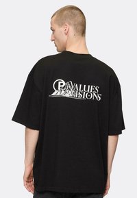 Tricou oversized negru din bumbac, cu un grafic alb al unei muntii și textul "VALORI VIZIUNI" pe spate. Mânici scurte și largi.