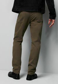 Khaki zwężane spodnie wykonane z gładkiego materiału. Posiadają kieszenie z tyłu i prosty krój nogawki, w połączeniu z czarnymi butami.