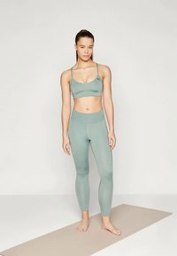 Ensemble de brassière de sport et leggings vert clair en tissu lisse et extensible, avec un logo sur la brassière et une coupe ajustée.