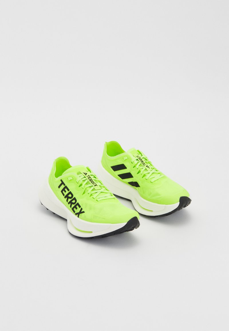Neonsko zelene sportske cipele s crnim detaljima, sa mrežastim gornjim dijelom, debelim bijelim međuslojem i "TERREX" oznakom sa strane.