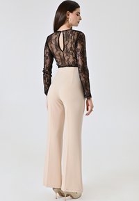 Zwarte kanten top met lange mouwen en een keyhole achterkant, gecombineerd met hoge beige flared pants. Gladde textuur, aansluitend ontwerp.