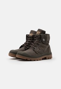 Botas de tobillo de lona marrón oscuro con punta de goma, cordones redondos, parche de logo lateral y suela de goma texturizada. Tacón plano con relieve resistente.