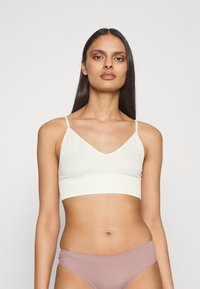 Haut court côtelé blanc avec de fines bretelles et un décolleté en V. Texture douce, forme ajustée, porté avec un bas de bikini rose clair.