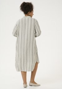 Abito camicia lungo a strisce in tessuto leggero, con strisce verticali grigie e bianche, caratterizzato da spacchi laterali e colletto con bottoni.