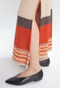 Svarta läderballerina skor kombinerade med en färgglad randig långkjol i stickat material som har segment i rött, orange, beige och grått.