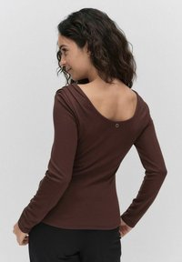 Brun långärmad topp med bred halsringning och subtil detalj på ryggen. Mjuk, elastisk tyg. Figursydd design framhäver silhuetten. Minimalistisk stil.