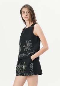 Svart ermeløs topp med hvite broderte palmetre-design, parret med matchende shorts som har lignende broderi-akcenter.