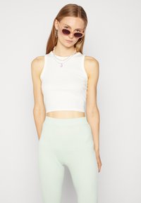 Top cropped branco com textura canelada, combinado com calças de cintura alta caneladas em verde menta. A modelo usa óculos de sol ovais cor-de-rosa e colares em camadas.