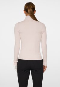 Długi rękaw, dopasowany, jasnoróżowy golf z prążkowaną teksturą, gładkim ciałem i dyskretnymi detalami szycia. Noszony z ciemnymi spodniami.
