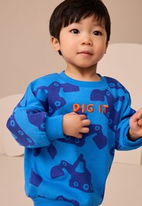 Blue cotton sweatshirt featuring a pattern of dark blue construction vehicles, with "DIG IT" embroidered in orange on the front.