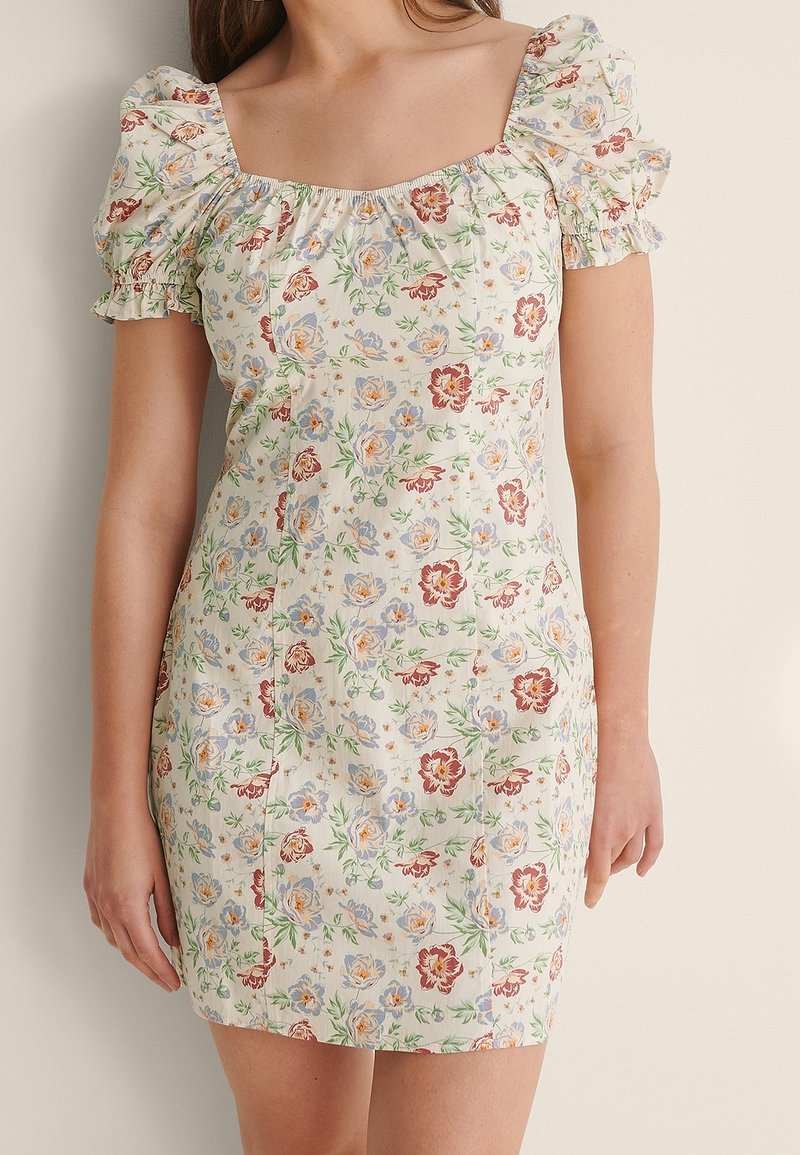 Robe mini à imprimé floral en tissu crème, avec des manches bouffantes, un décolleté carré et des motifs de fleurs multicolores avec des feuilles vertes.