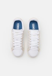 White sneakers with beige accents, textured mesh and leather upper, round toe, laces, and blue cushioned insole with logo.