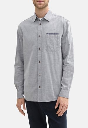 Chemise grise à manches longues avec un motif texturé, devant boutonné, boutons marron et une poche poitrine unique avec un accent bleu.