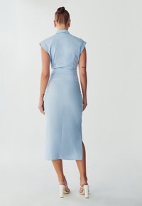 Hellblaues tailliertes Kleid mit kurzen Ärmeln, einem Kragen und einem mittellangen Saum, ausgestattet mit einem seitlichen Schlitz und einer glatten Stoffoberfläche.