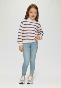 Gebreide trui met crèmekleurige en paarse strepen, hoge kraag, gecombineerd met lichtblauwe skinny jeans en meerkleurige sneakers.