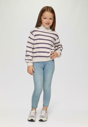 Pull en tricot avec des rayures crème et violettes, col montant, associé à un jean skinny bleu clair et des baskets multicolores.