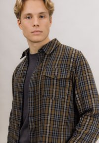 Brun og svart rutete skjorte med knapper, med en enkelt brystlomme, laget av mykt stoff, med krage og avslappet passform.