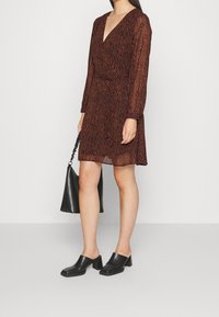 Klädsel i djurmönster med bruna nyanser, v-ringad, långärmad och med cinchad midja. Matchas med en svart handväska och blockklackade mule-skor.